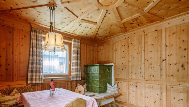 Une pièce chaleureuse avec des murs et un plafond en bois, un meuble vert, un tapis à motifs et une table recouverte d’une nappe rose.