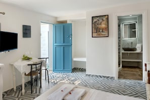 A hotel room with a dining area, a blue door, a bathroom with a mirror, and patterned flooring.