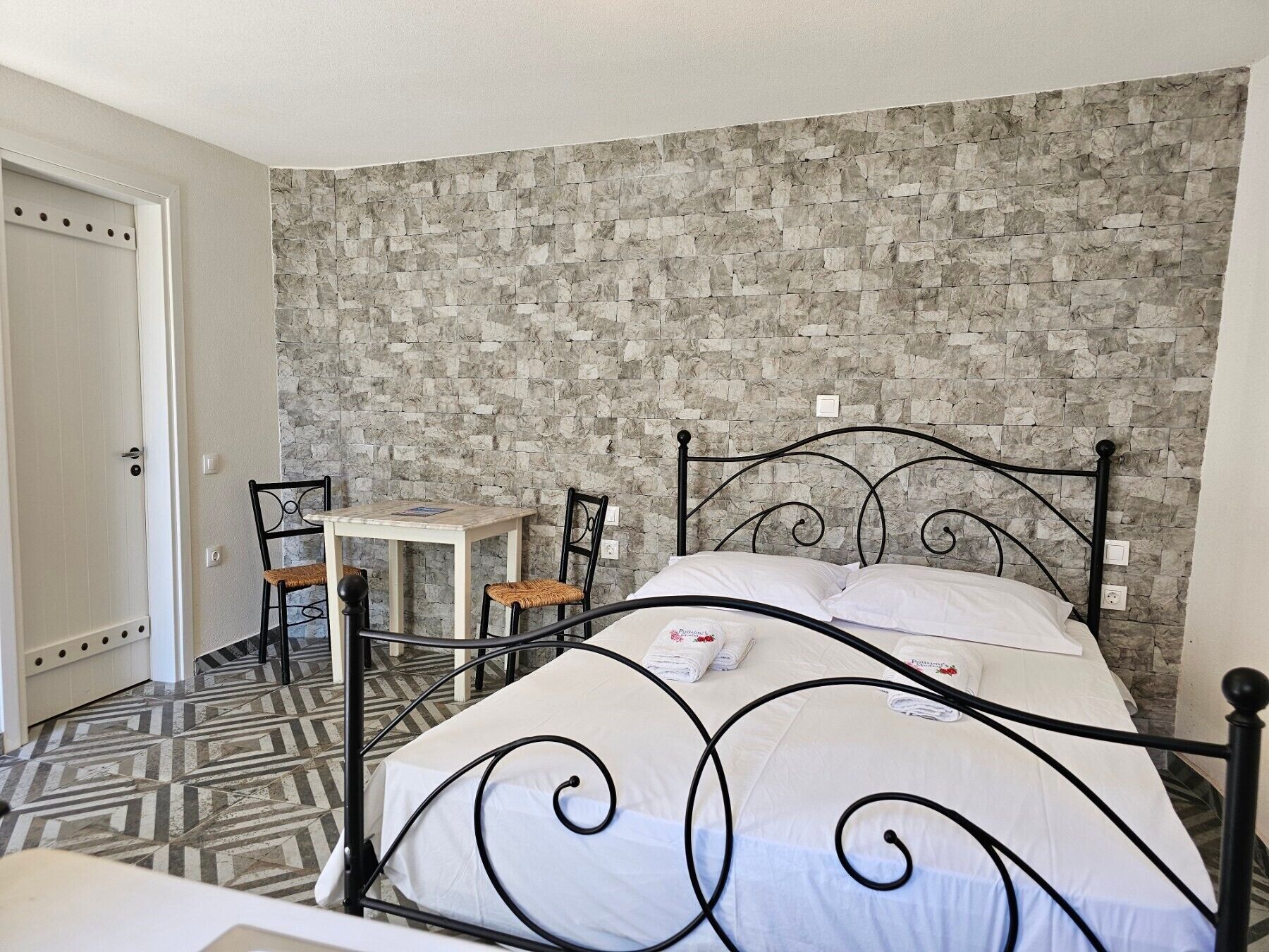 Une pièce comprenant un lit, une petite table, deux chaises et un sol à motifs.