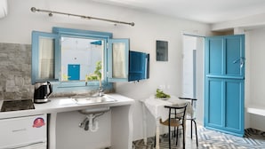 Una cocina compacta con un lavamanos, un hervidor, una mesita con una silla y un armario azul.