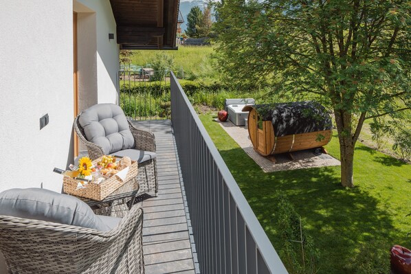 A balcony with wicker furniture, a wooden sauna, and a grassy garden. - Apartment 'Alpenrose' with Mountain View, Shared Terrace and Wi-Fi (St. Martin in Gsies)