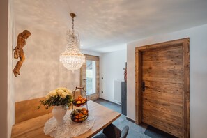 A dining area with a wooden table, a chandelier, a vase with flowers, and a fruit basket.