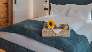 Un lit avec une couverture bleue, des oreillers blancs et un panier de fruits, ainsi qu’un tournesol.