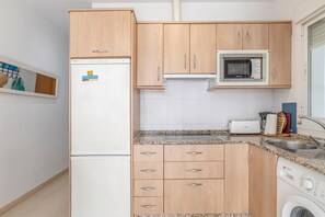 Une cuisine compacte avec des meubles en bois, un four à micro-ondes encastré, un réfrigérateur, un lave-linge et un petit plan de travail avec un évier.