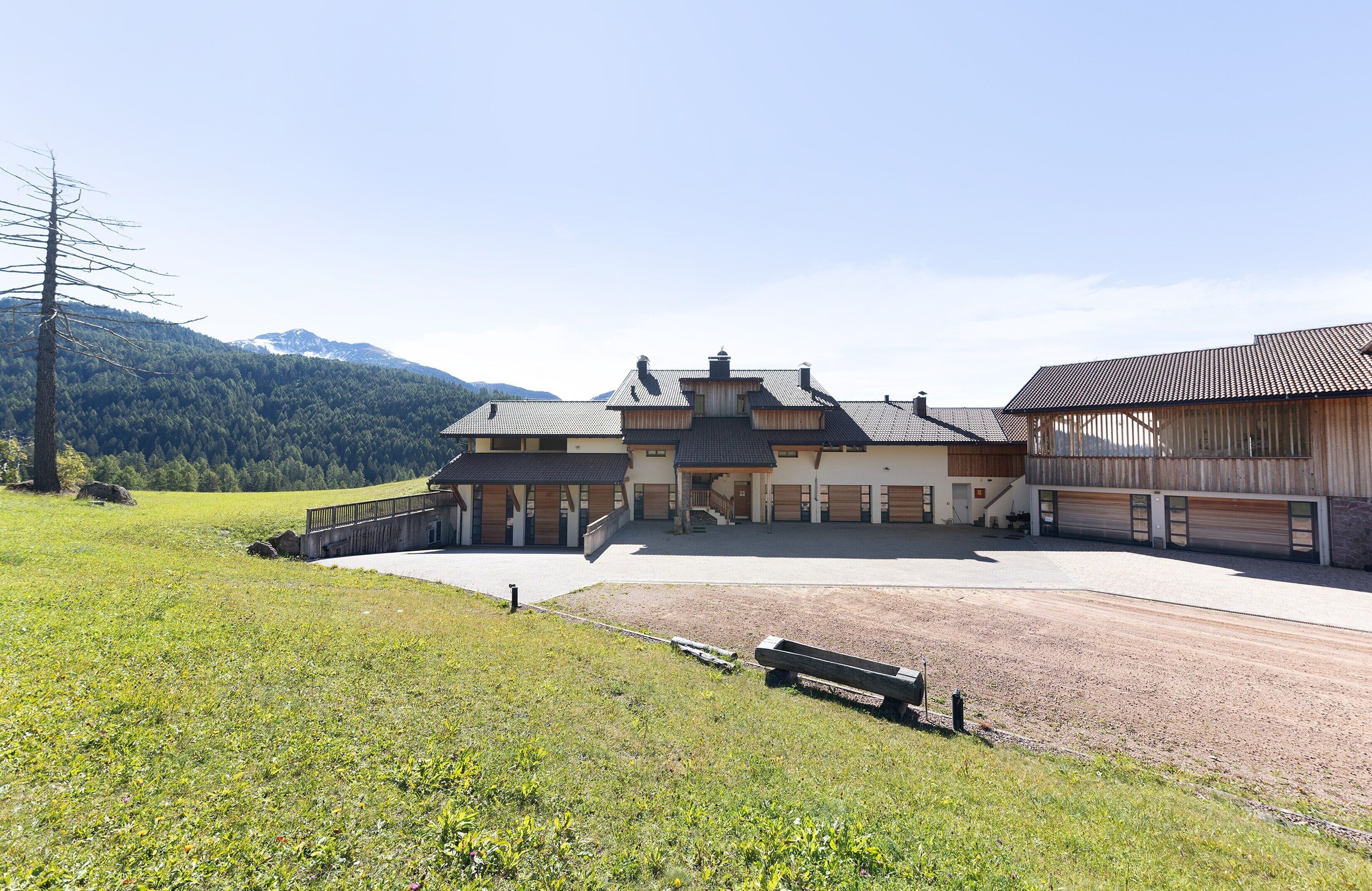 A large building with multiple garage doors, a covered driveway, and a grassy area with a bench.