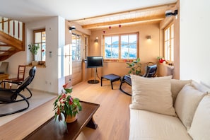 A living room with a sofa, a television, a wooden staircase, and a window with a view of a snowy landscape. - Holiday Home 'Lexn Radein' with Mountain View, Wi-Fi and Air Conditioning (Radein)