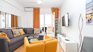 Una sala de estar moderna con sofá, sillones, una mesa de centro de vidrio, televisor y un balcón con vistas.