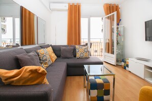 Uma sala de estar moderna com um sofá seccional, uma mesa de centro de vidro e um armário branco com uma TV.