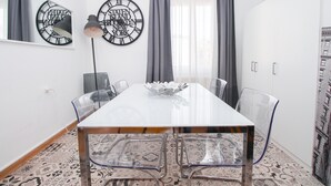 Un comedor moderno con una mesa blanca, sillas transparentes y relojes decorativos en la pared.