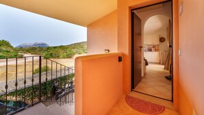 Uma varanda com guarda-corpo de metal, vista para uma montanha e cozinha visível por uma porta aberta.
