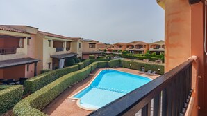 Un quartier résidentiel doté d’une piscine, entourée d’arbustes soigneusement taillés, et d’un balcon donnant sur la piscine.