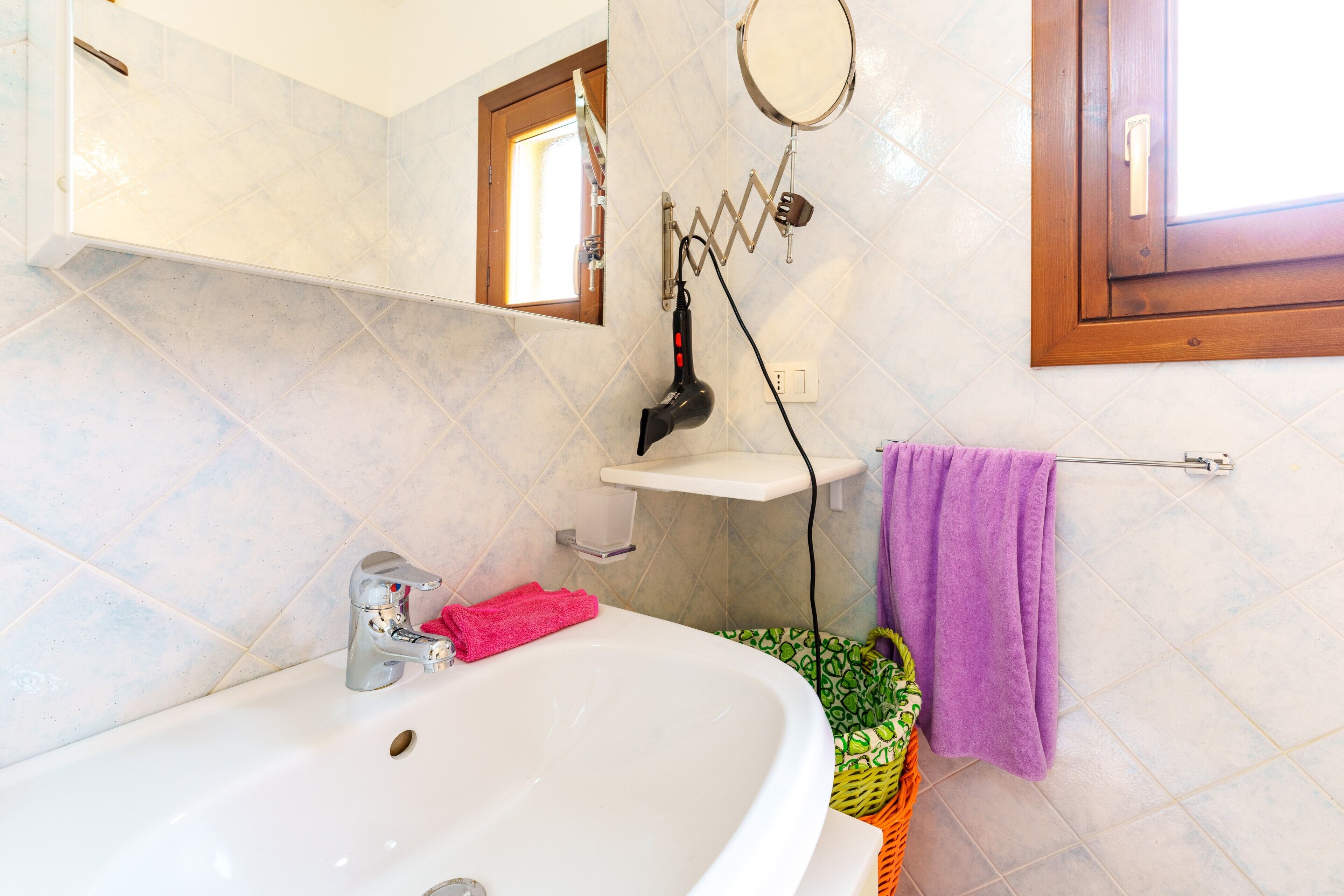 A bathroom with a white sink, a mirror, a hairdryer, a purple towel, and a window.