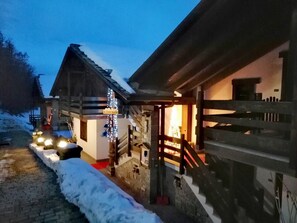 A wooden building with a staircase and a lit interior, surrounded by snow.