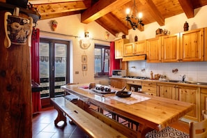A wooden kitchen with a large table, wooden cabinets, and a view through the window.