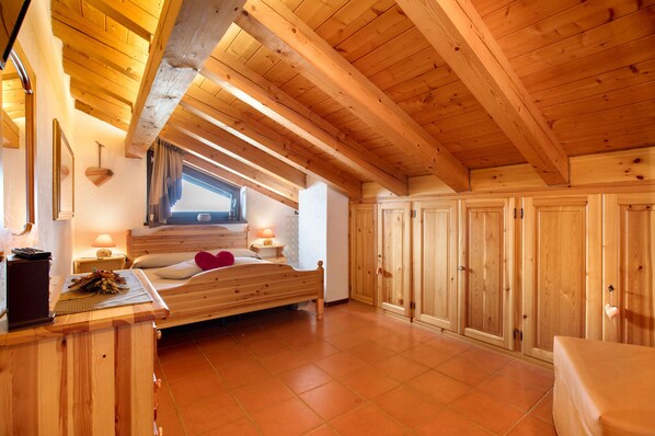 A wooden room with a bed, a nightstand, a wardrobe, and a window.