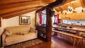 A cozy loft-style room with a wooden ceiling, a sofa, a dining table, and a kitchen area. - Apartment 'Elois' with Mountain View, Shared Terrace and Wi-Fi (Gressan)