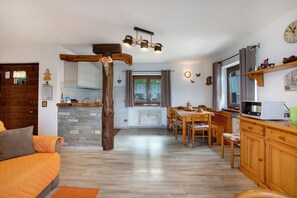 Uma sala de estar aconchegante com um sofá de madeira, uma área de jantar com mesa e cadeiras, uma cozinha com micro-ondas e uma janela grande.