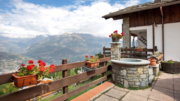A terrace with a stone fountain, wooden railing, and potted plants. - Apartment 'Sylvie' with Mountain View, Shared Terrace and Wi-Fi (Gressan)