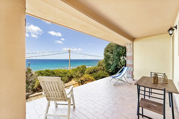 A patio with a view of the ocean, a table with chairs, and a hammock.