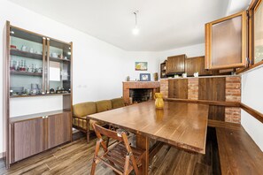 Un comedor con mesa de madera, sillas, chimenea de ladrillo y una alacena empotrada con puertas de cristal.
