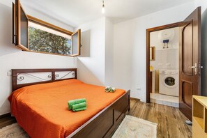 Un dormitorio con cama, ventana con vistas, lavadora y puerta de madera.