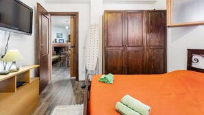 A room with a bed, a TV, a wooden wardrobe, and a desk with a lamp. - Aventino Gutturu Holiday Home with Sea View, Private Terrace and Garden (Gutturu)