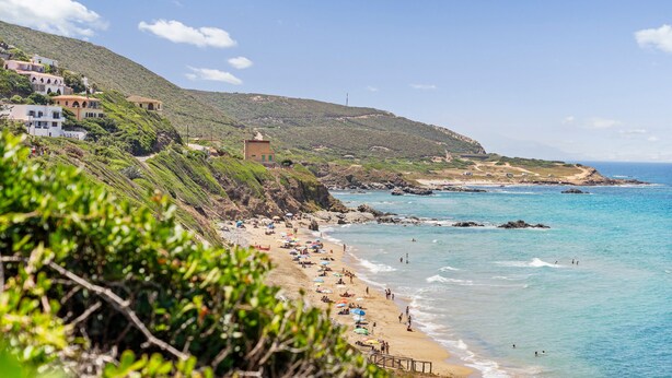 A coastal beach with buildings on a hillside, clear blue water, and a rocky shoreline. - Aventino Gutturu Holiday Home with Sea View, Private Terrace and Garden (Gutturu)