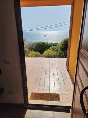 A doorway leading to a tiled patio with a 'WELCOME' mat and a view of the sea. - Aventino Gutturu Holiday Home with Sea View, Private Terrace and Garden (Gutturu)