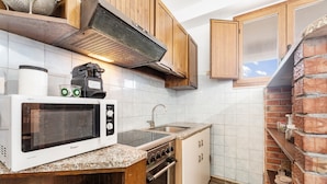 A compact kitchen with a microwave, stove, sink, and wooden cabinets. - Aventino Gutturu Holiday Home with Sea View, Private Terrace and Garden (Gutturu)
