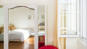 A bedroom with a bed, a small table, a chair, and a window.