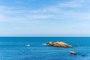 A coastal scene with a boat, a rocky outcrop, and calm blue waters.