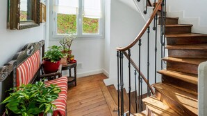 A staircase with wooden steps and black balusters, a wooden bench with a red cushion, and a window with a view of greenery.