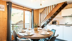 Un intérieur en bois avec une table de salle à manger ronde, disposée pour accueillir six personnes, un escalier et un coin cuisine.