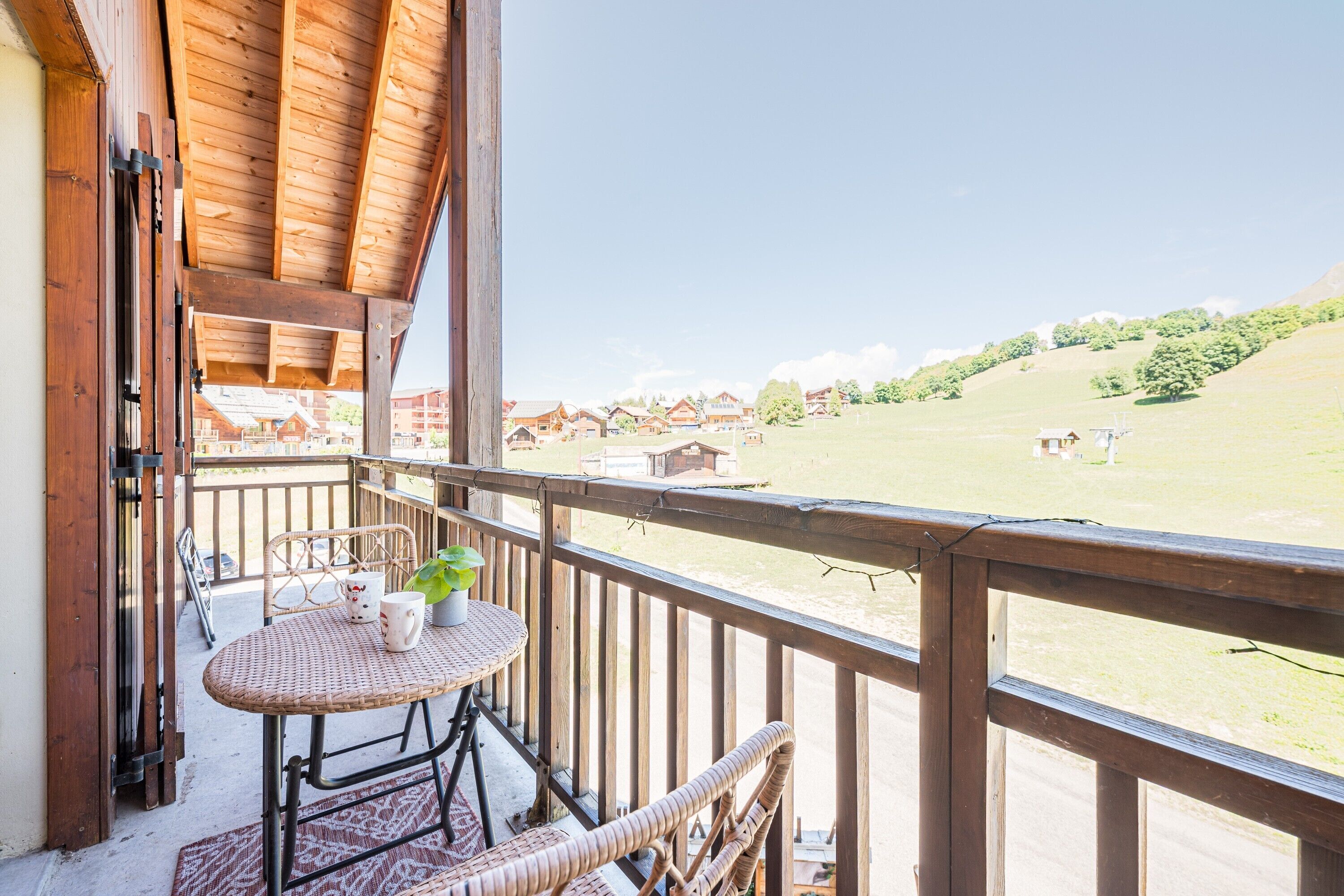 A balcony with wicker furniture, a table, and a view of a grassy area with buildings in the distance.