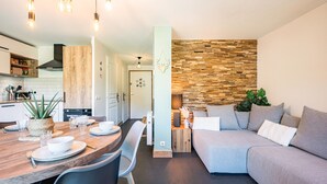 Une cuisine moderne avec des meubles en bois, une table à manger pour quatre personnes et un coin salon avec un canapé gris et un mur en bois.