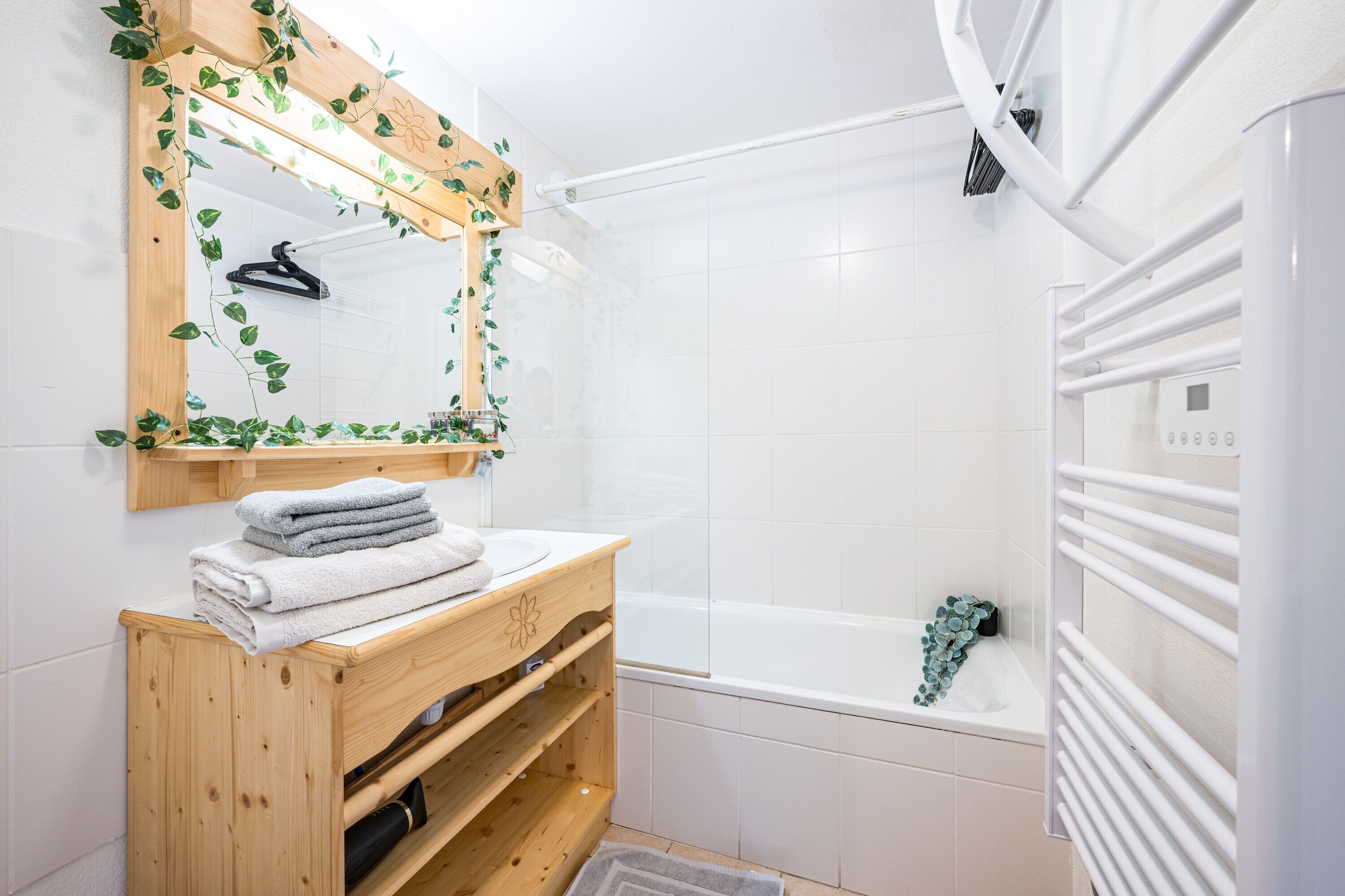 A bathroom with a wooden vanity, a white bathtub, and a mirror with a wooden frame.