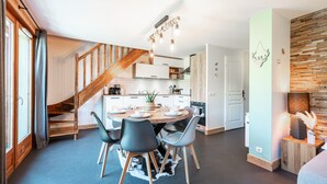 Une cuisine moderne avec un coin repas, un escalier en bois et un mur d’accent en pierre.