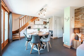 Une cuisine moderne avec un coin repas, un escalier en bois et un mur d’accent en pierre.