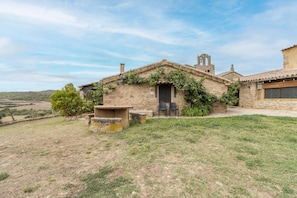 A rustic stone house with a stone patio, two chairs, and a small table.