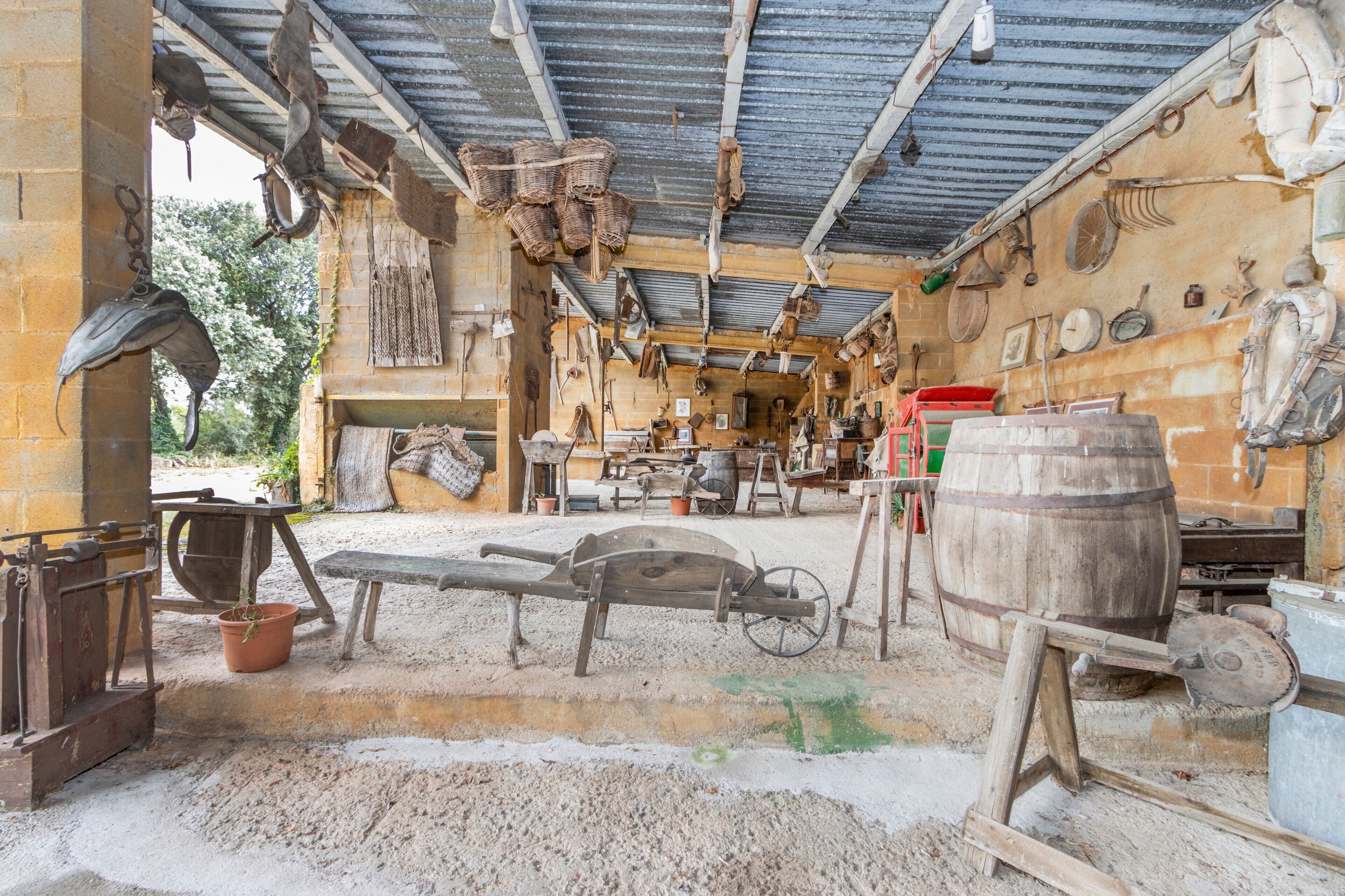 Ein rustikales Interieur mit Holzboden, einem großen Holzfass und verschiedenen Werkzeugen und Geräten.