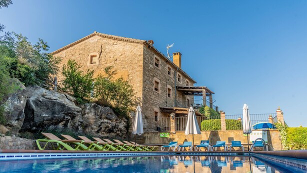 A stone building with a pool, lounge chairs, and umbrellas.