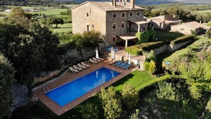 A stone building with a swimming pool and lounge chairs.