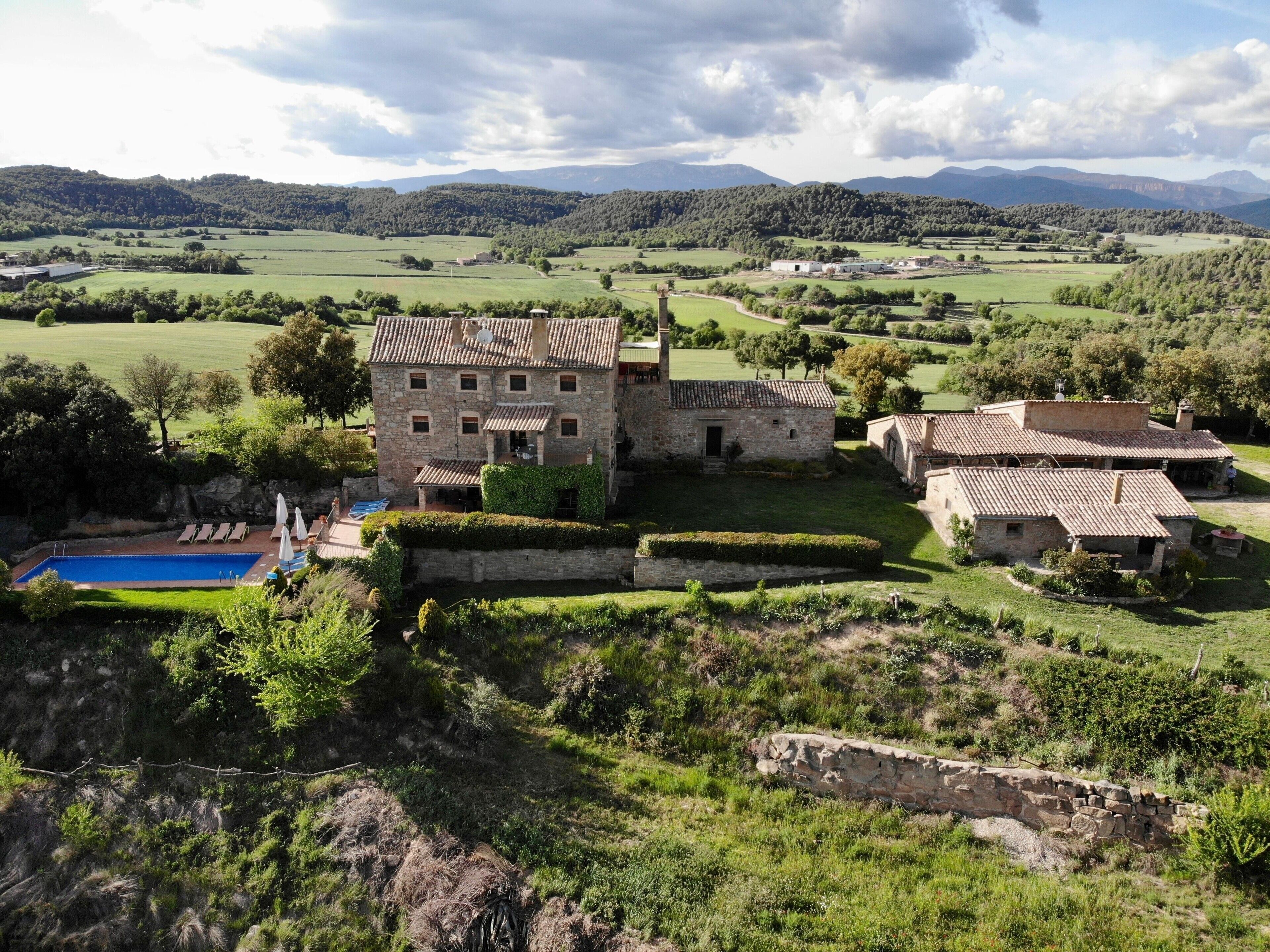 A stone building with a pool, surrounded by lush greenery and hills.