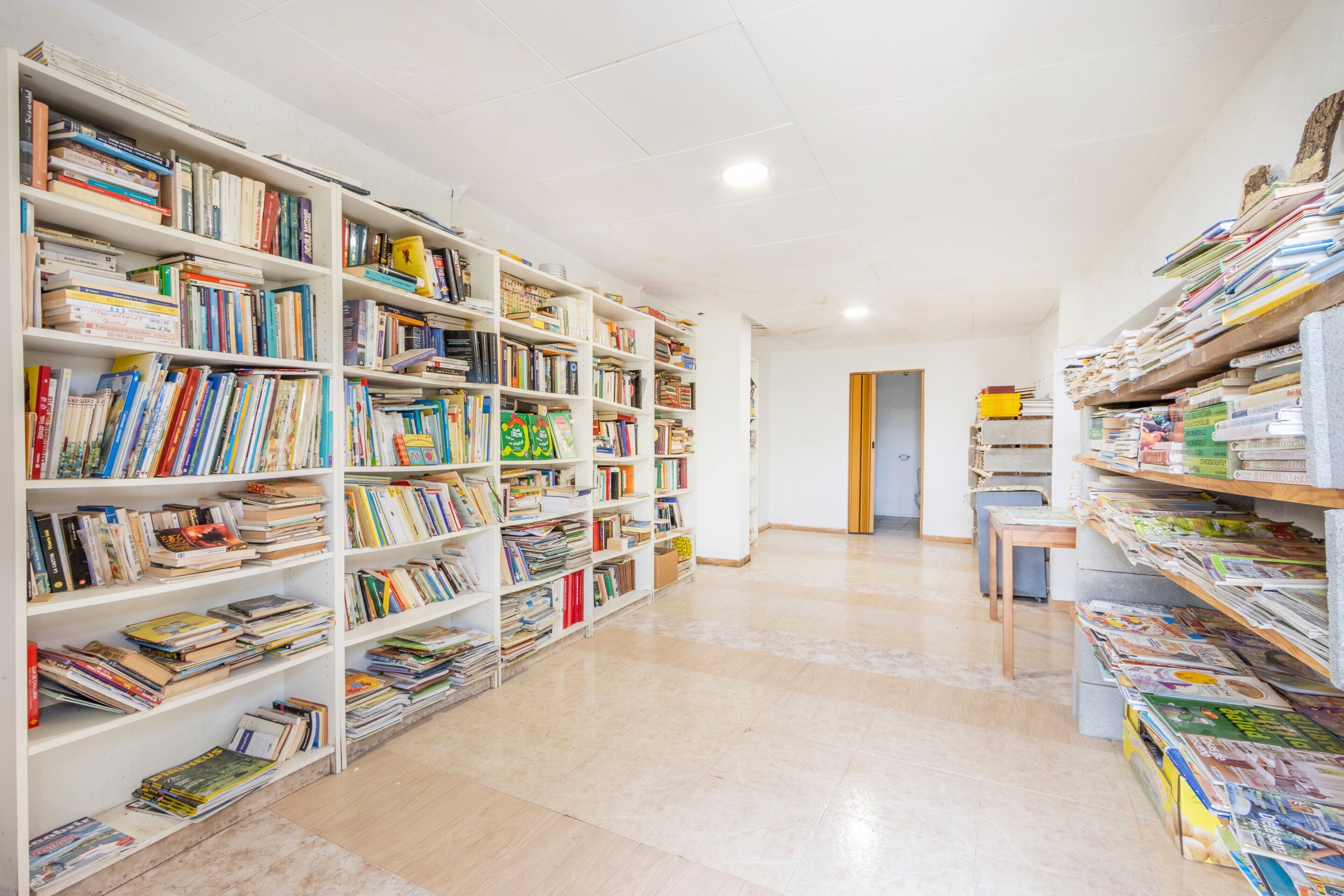 A library with bookshelves filled with books, a wooden table, and a door in the background.