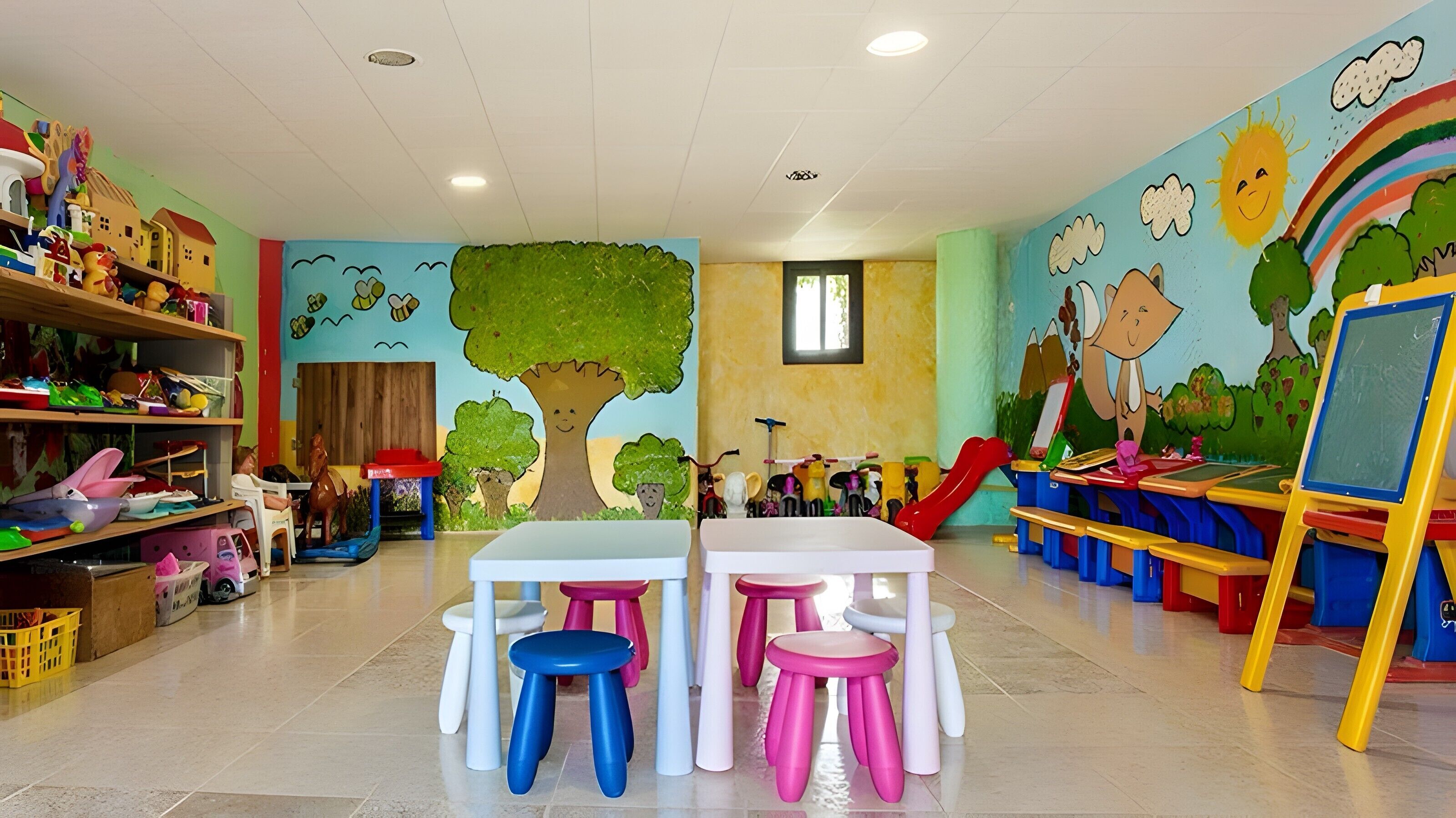 Ein Spielzimmer für Kinder mit Tischen, Hocker und Spielzeug.