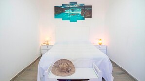 A narrow hotel room with a bed, two bedside tables, a wall-mounted painting, and a small bedside lamp. - Holiday Home 'Villa Sunset' with Sea Views, Wi-Fi and Air Conditioning (Calafell)