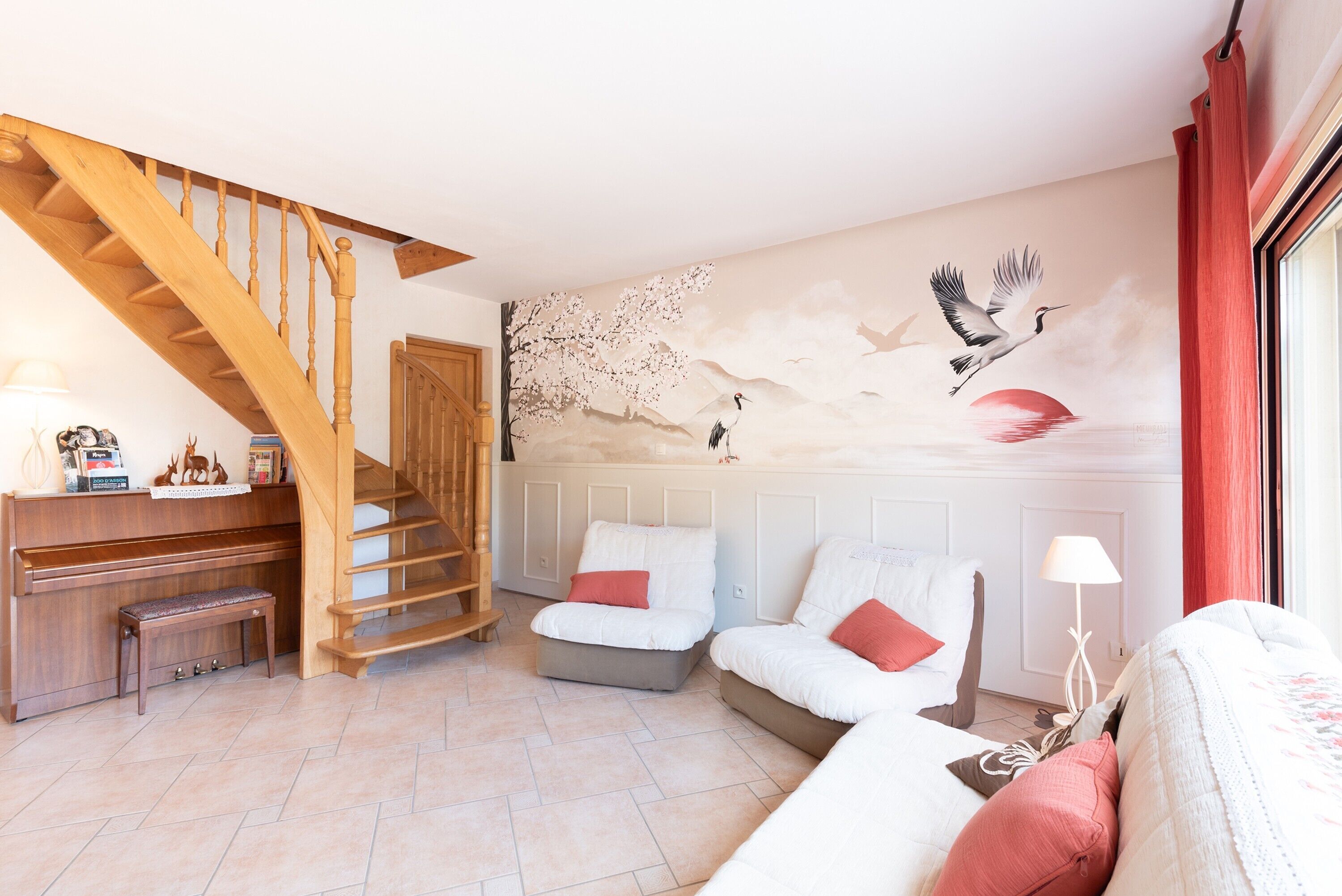 Ein Wohnzimmer mit einer Holztreppe, weißen Sofas, einem Klavier und einem Wandgemälde.