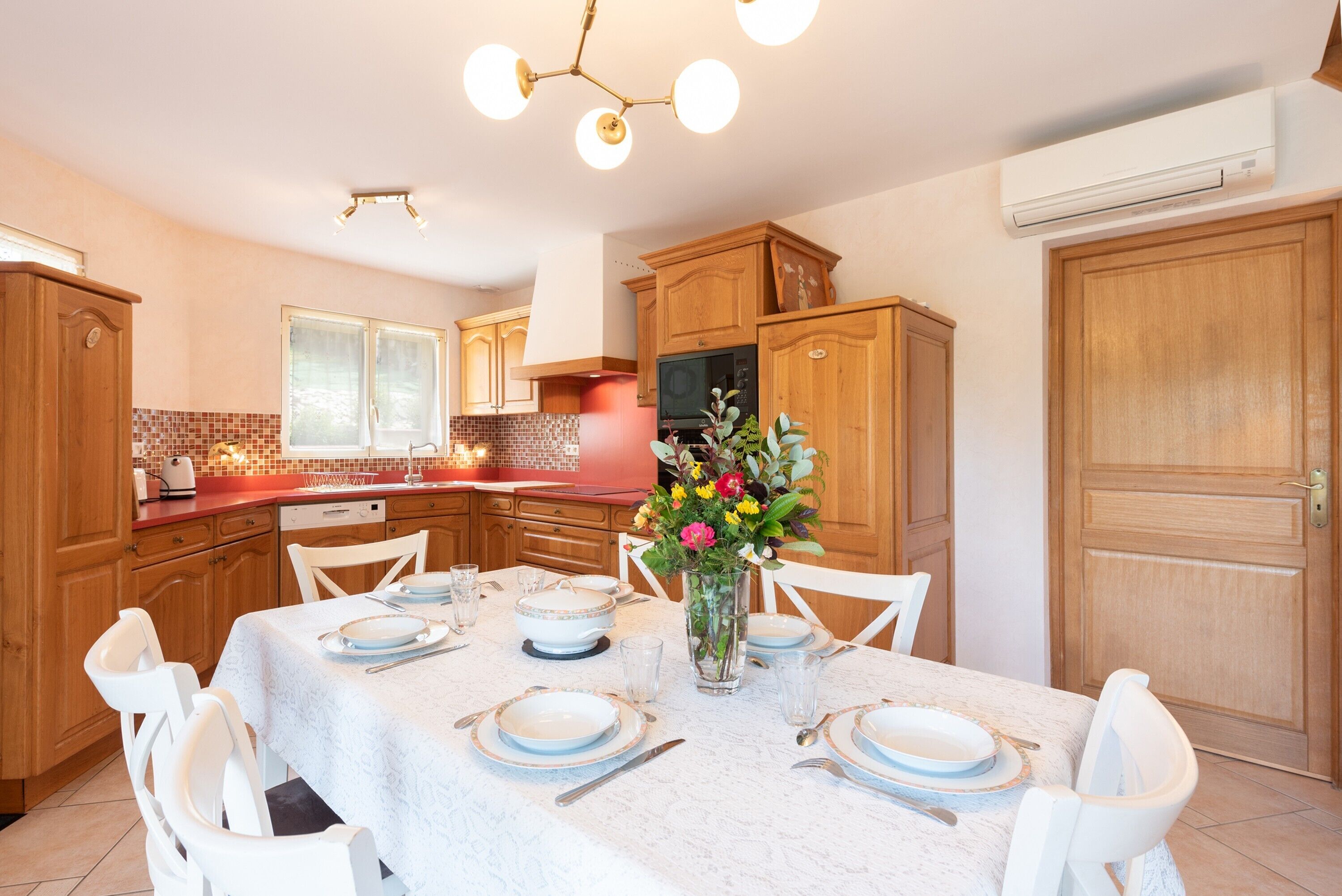 A modern kitchen with wooden cabinets, a dining table set for four, and a vase with flowers.