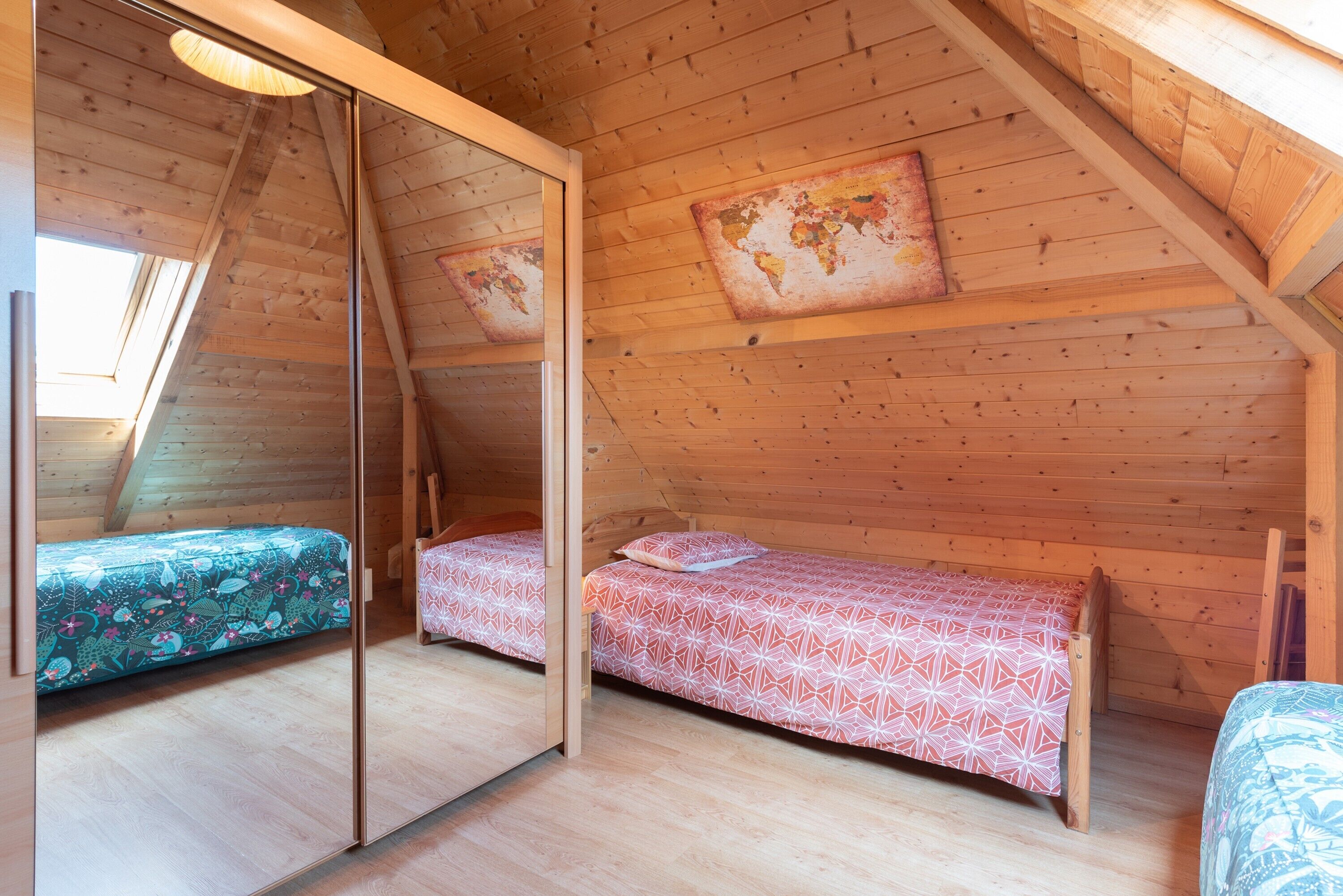 A wooden cabin with two beds, a world map on the wall, and a sloped ceiling.