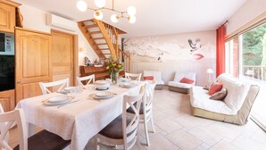 A dining area with a table set for four, a staircase, a sofa, and a mural on the wall. - Zen House in the Pyrenees, Private Terrace and Wi-Fi (Coarraze)